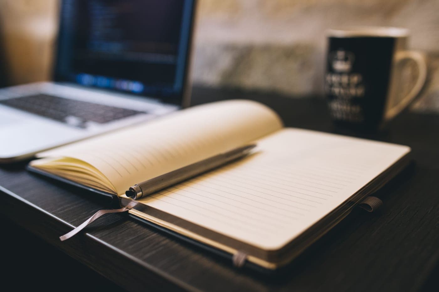 An open notebook with a pen and a cup of coffee
