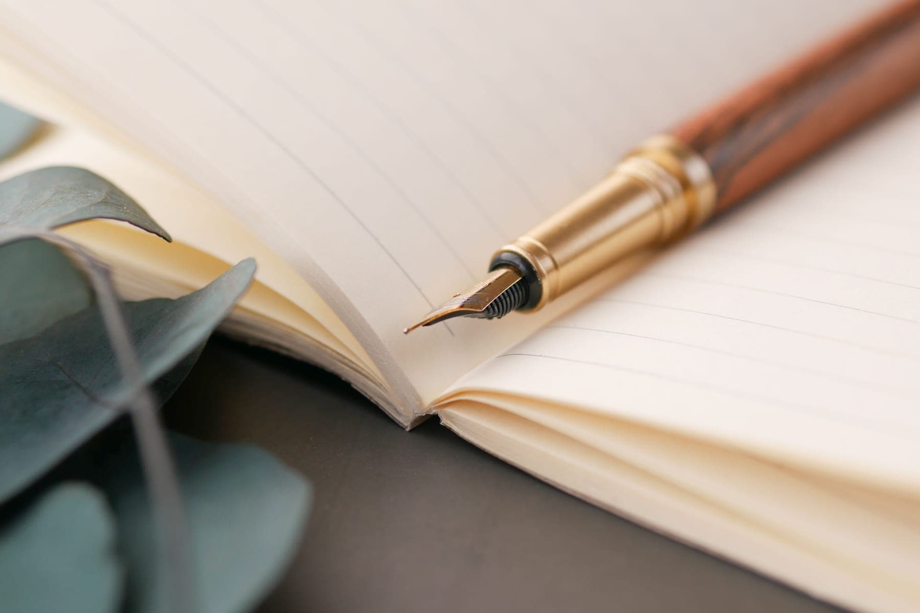 A fountain pen writing in an open notebook on a wooden desk